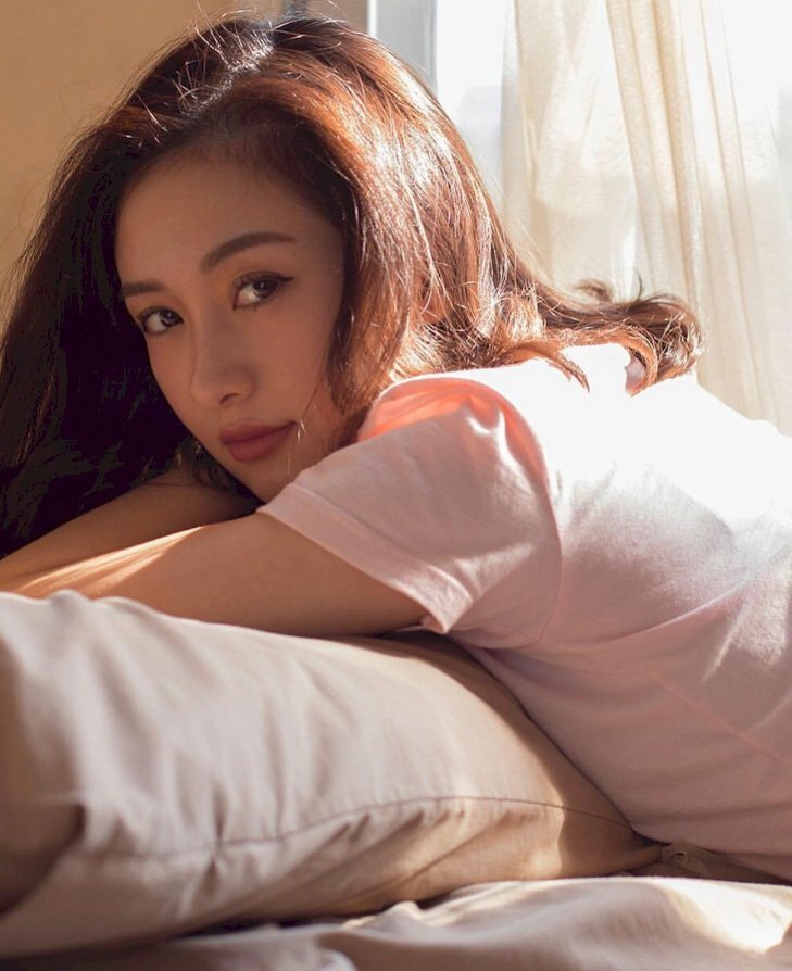 Tạo dáng chụp ảnh trên giường cuốn hút và dễ thương với góc chụp nửa người, cô gái trong tư thế nằm sấp tựa càm trên tay mặt quay ngang nhìn ống kính, miệng cười nhẹ