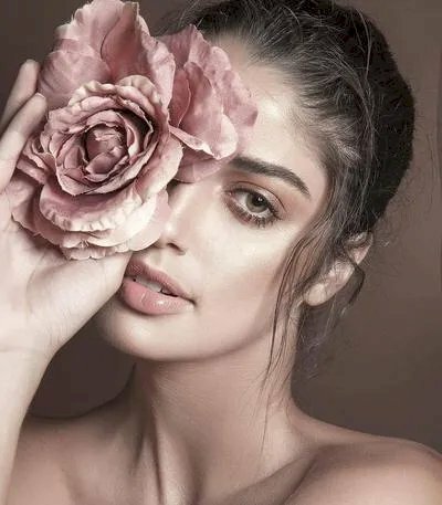 Tạo dáng cô gái xinh đẹp với đôi mắt cuốn hút cùng bông hoa hồng che môt bên mắt, đầu hơi nghiêng, mắt nhìn thẳng ống kính