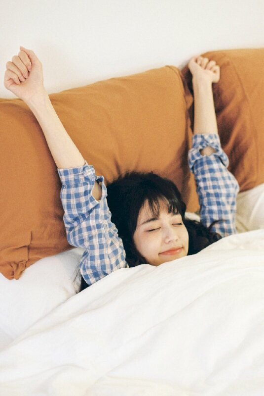 Tạo dáng khỏe khoắn rất cute với 2 tay dơ cao, mắt nhắm miệng cười nhẹ với tư thế vẫn còn nằm trên giường trông rất tự nhiên