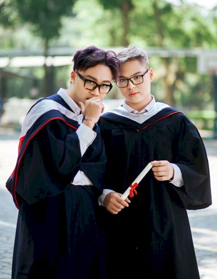 Tạo dáng đẹp chụp ảnh kỷ yếu cho 2 nam sinh viên trong bộ đồ cử nhân với dáng đứng thẳng mắt cùng nhìn về một hướng, một người đứng nghiêng, một người đứng trực diện