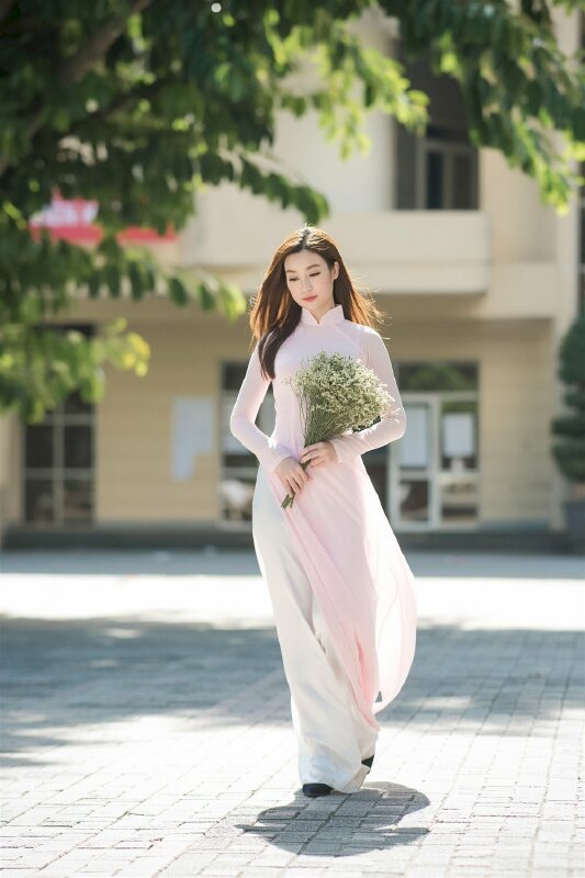 Tạo dáng đẹp, đáng yêu với nét diễn bước đi tự nhiên 2 tay cầm bó hoa dại trắng, đầu hơi cúi, mắt nhìn xuống cùng hiệu ứng tóc bay