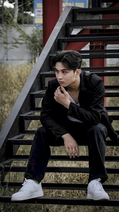 Cách tạo dáng chụp ảnh với cầu thang dành cho nam cực ngầu với dáng ngồi dang rộng hai chân đặt lên bậc thang, 1 tay đưa lên chạm vào cằm, 1 tay đặt trên đùi và người hơi khom lên phía trước.