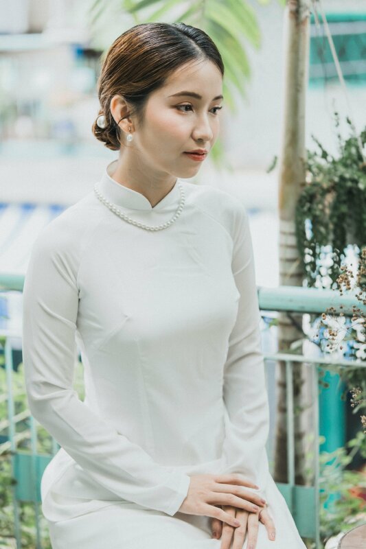 Dáng ngồi tự nhiên, 2 tay đặt lên đuồi, người hơi nghiêng, mắt nhìn xa xăm phảng phất nét đuộm buồn thời học sinh