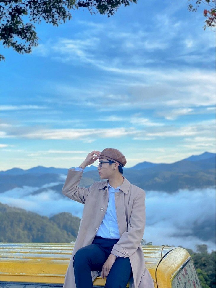 Kiểu tạo dáng cực hút cho nam khi đi Đà Lạt với một tay đặt lên đùi tay còn lại chạm nhẹ lên nón dáng ngồi thong dong giữa đất rừng cao nguyên và bâu trời xanh mát