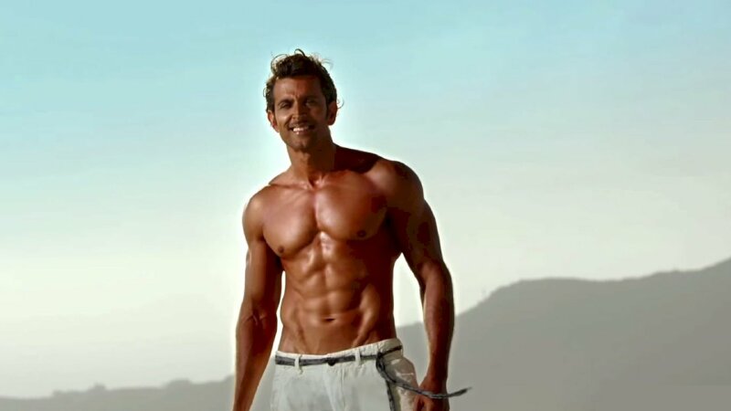 Kiểu tạo dáng đứng tự nhiên lộ cơ thể sáu múi và làn da hơi rám nắng, miệng cười tươi