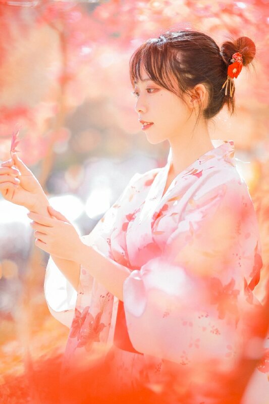 Cách tạo dáng đẹp cho các bạn nữ trong chiếc áo Kimono màu hồng với góc chụp một bên, một tay cầm chiếc lá phông, mắt nhìn là phônh, miệng cười nhẹ