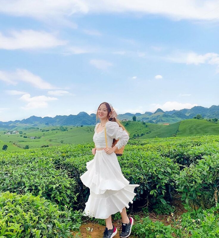 Tạo dáng hồn nhiên vui tươi trong chiếc váy trắng tinh, 2 vai mang gùi, đầu đội khăn tạo nét phong cách dễ thương, miệng cười tươi