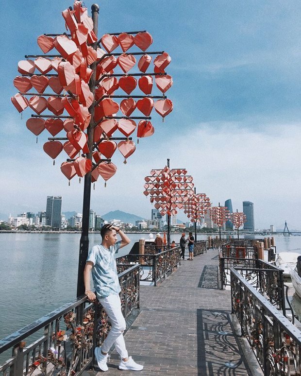 Cách tạo dáng chụp ảnh ở cầu Tình Yêu dành cho nam, hãy tìm đến và đứng dưới cây cột có treo lòng đèn trái tim, đứng tựa lưng vào thành cầu, 1 tay cầm lên thành cầu, 1 tay đưa lên vuốt tóc, đặt 1 chân co nhẹ lui sau chạm vào thành cầu, 1 chân thẳng, với góc chụp nghiêng bạn sẽ có được bức ảnh đẹp.