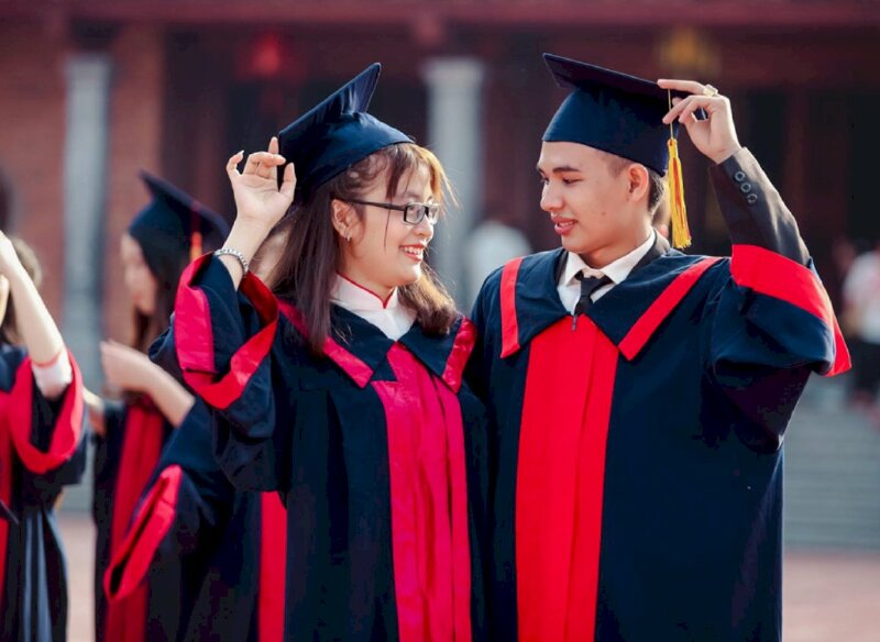 Tạo dáng chụp ảnh tốt nghiệp với người yêu dễ thương với dáng đứng 2 người nhìn nhau cười, 1 tay chạm nhẹ nón, người tựa vào nhau