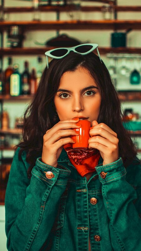 Tạo dáng cô gái với nét diễn dễ thương cùng đôi mắt to tròn trong trẻ với chiếc áo jean năng động, 2 tay nâng tách cafe màu đỏ lên miệng, mắt nhìn thẳng ống kính