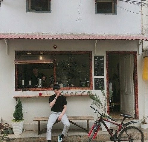 Tạo dáng nam trước quán cafe cũ kỹ với 1 tay đang chạm điếu thuốc, 1 tay đặt lên đùi rất đàn ông với thần thái chill nhẹ