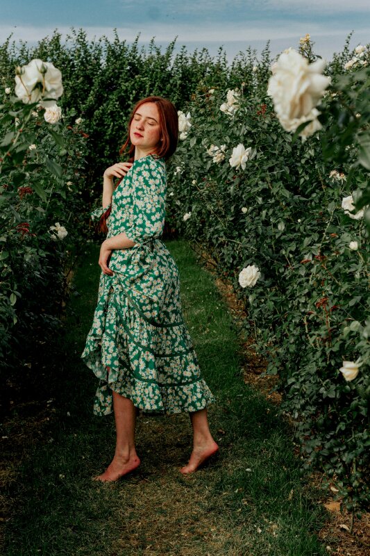 Tạo dáng tỏa nét đẹp trong trẻo hồn nhiên dưới nắng nhẹ trong chiếc đầm hoa màu xanh, một chân bướ lên trước, 1 tay nắm váy, 1 tay chạm ngực, người quay nghiêng, mắt nhắm nhẹm mặt hơi ngước trong vườn hoa xinh đẹp