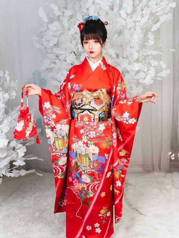 Tạo dáng đứng tự nhiên đẹp trong bộ áo Kimono màu đỏ tươi, một tay cầm chiếc túi đỏ nhỏ, 1 tay đưa lên tạo dáng, mắt nhìn ống kính