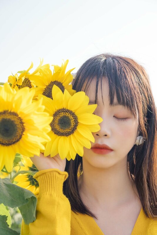 Cách tạo dáng đẹp với hoa hướng dương to che một bên mặt với góc chụp cận mặt, mắt nhắm tự nhiên