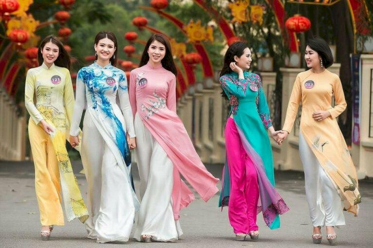 Cách tạo dáng chụp ảnh áo dài tập thể kiểu tự nhiên dành cho nhóm 5 người, xếp thành 1 hàng ngang cùng bước đi, 1 nhóm gồm 3 người nắm tay nhau cùng nhìn thẳng vào ống kính và nhóm gồm 2 người nắm tay bước đi và trò chuyện vui vẻ với nhau.