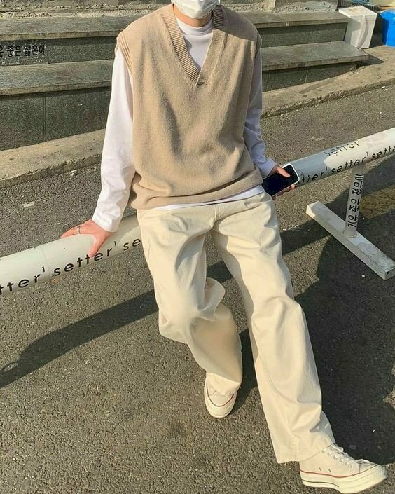 Trang phục áo thun tay dài bên trong kết hợp áo ghi lê bên ngoài cùng với chiếc quần suông rộng màu trắng, với dáng ngồi tựa, hai tay đặt cầm 2 bên sẽ giúp bạn nam gầy có 1 dáng chụp hình đẹp và trông không bị gầy.