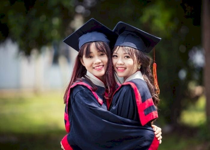 Cách tạo dáng chụp ảnh áo cử nhân kỷ yếu đôi bạn thân nữ, đang ôm eo nhau, 2 gương mặt cùng quay về phía ống kính và cười tươi