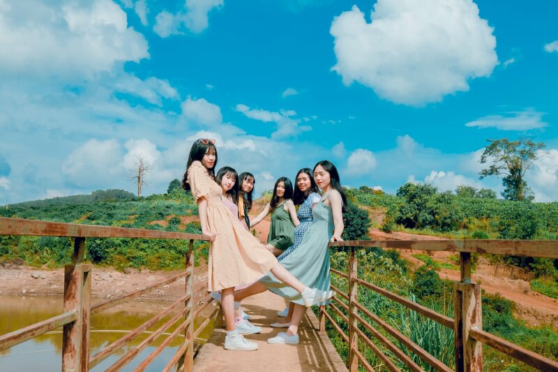 Tạo dáng chụp ảnh trên cầu khi đi chơi cùng nhóm bạn với tư thế đưa cao một chân, đứng quay người vào nhau, miệng cười tươi, mắt nhìn ống kính