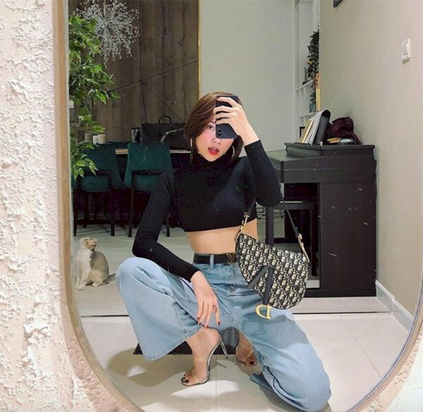 Cách chụp ảnh với áo croptop dài trước gương với dáng ngồi ngầu chất, với kiểu này hãy ngồi xổm quỳ gối bằng 1 chân, và chân còn lại đặt hướng ra ngoài, 2 đầu gối tạo hình chữ V, 1 tay đặt trên đùi và 1 tay cầm điện thoại đưa lên chụp hình.