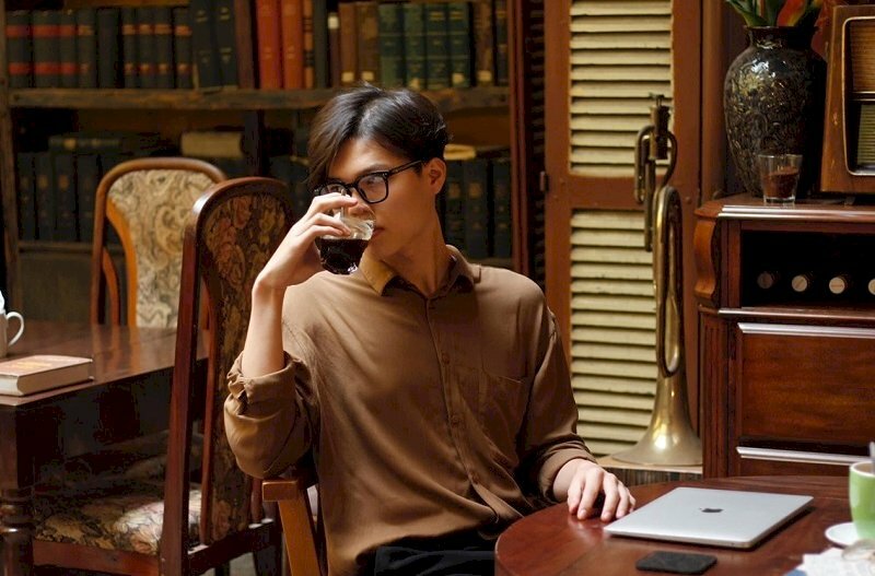 Cách tạo dáng nam thần đang suy tư một tay cầm quyển sách, mũi lưỡi trai đội ngược chân bắt chéo chữ ngũ