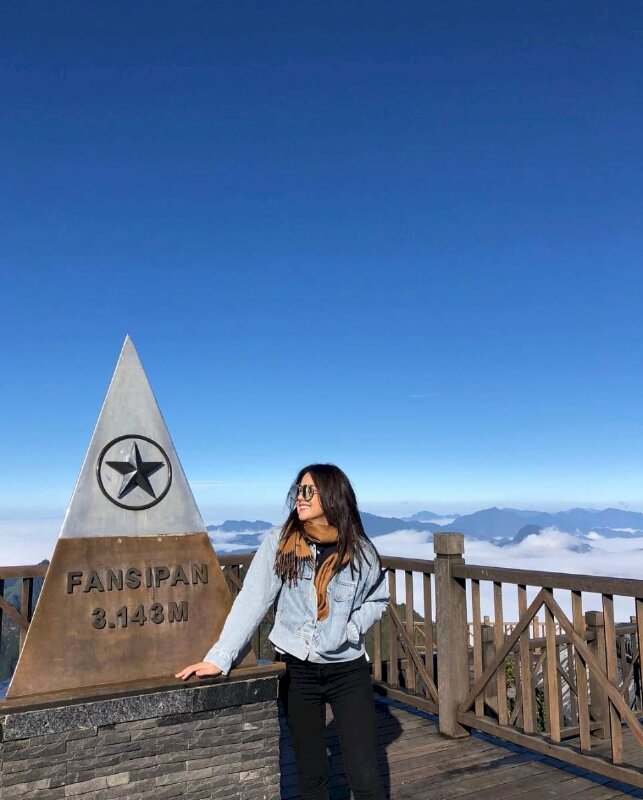 Tạo dáng tự nhiên đơn giản với với một tay ỏ vào túi áo, một tay chạm lên bục, mặt quay ngang, miệng cười tươi tỏa nét cá tính với đôi kính đen