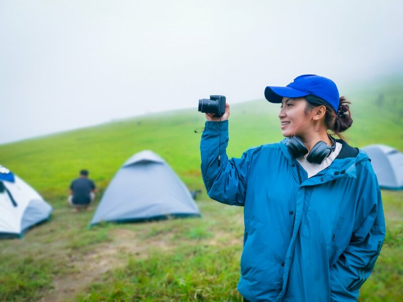 Kiểu tạo dáng đầy phong cách với chiếc máy ảnh cùng bộ thời trang style màu xanh dương, một tay đặt vào túi áo, một tay cầm máy ảnh, mặt nhìn nghiêng, miệng cười tươi