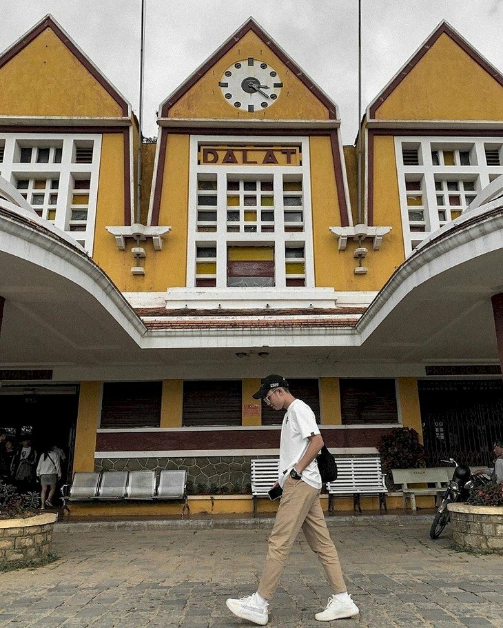 Kiểu tạo dáng nam trong chiếc quần kaki nâu cùng đôi giày sneaker đang bước đi với vẻ người hơi cúi xuống trên con đường của Đà Lạt