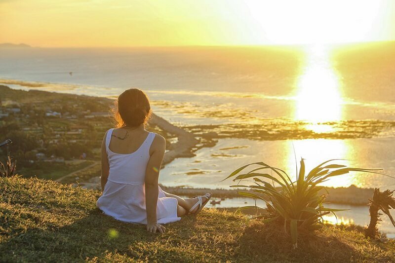 Tạo dáng chụp ảnh chờ bình minh trên biển của cô gái trong chiếc đầm trắng đơn giản với tư thế ngồi thẳng bắt chéo chân, 1 tay chống phía sau tạo nét đẹp tự nhiên