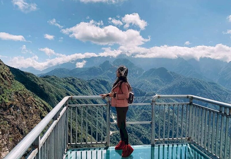 Cách tạo dáng đẹp của cô gái trên cầu kính Rồng Mây với phong cách cực chill trong dáng đứng nghiêng, mắt nhìn xa, một tay chạm thành cầu, một tay cầm vạt áo