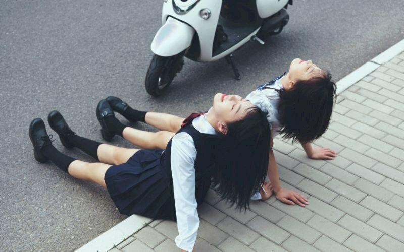 Tạo dáng chụp ảnh đôi bạn thân nữ ngồi trên đường, duỗi thẳng châm hai tay chống ra sau với người ngả ra phía sau, đầu ngước lên nhìn trời.