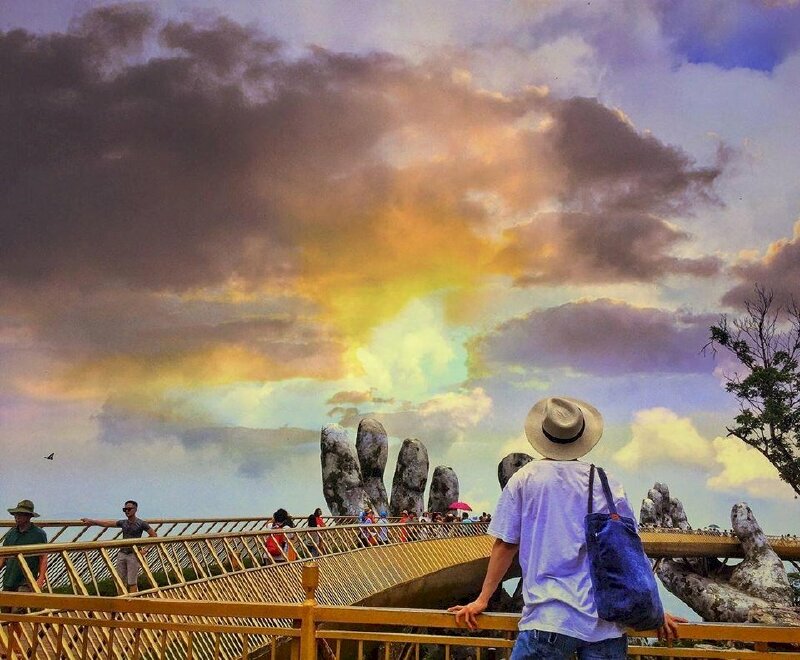 Cách tạo dáng chụp ảnh ở cầu Vàng đứng quay lưng vô cùng đẹp, với cách này bạn hãy lựa chọn nơi đứng chụp để thấy xa xa có hai bàn tay khổng lồ đang nâng đỡ cầu, và hãy đứng quay lưng lại với ống kính, đứng quay lưng và chống hai tay lên thành cầu, mặt như đang ngước nhìn xa xa về hai bàn tay, như vậy bạn sẽ có được tấm ảnh chụp tuyệt đẹp vừa lấy hết được 2 bàn tay, vừa lấy được hình cầu vàng mà cảnh bầu trời.