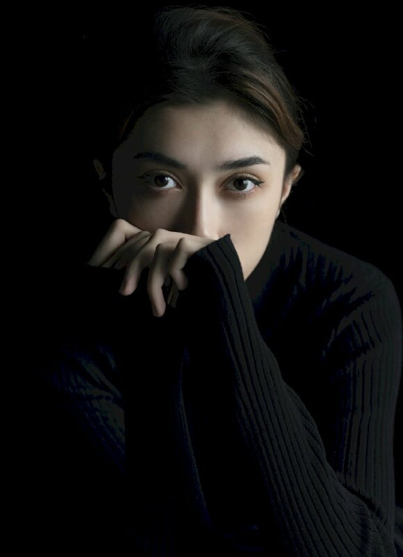 Tạo dáng chất nhất trên nền background màu đen với một tay che mặt, mắt hướng nhìn ống kính