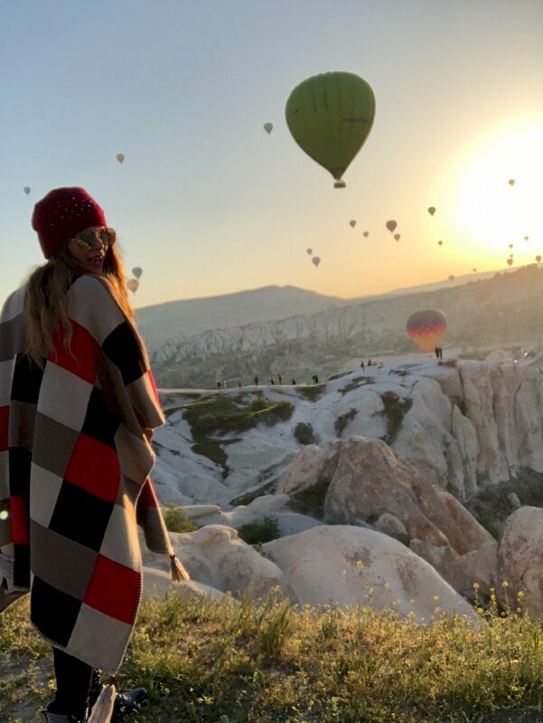 Tạo dáng đơn giản mà đẹp tự nhiên với góc chụp từ sau lưng của cô gái khoác chiếc khăn caro, đầu đội nón len, mang kính râm đứng quay người về phía bình mih cùng vô số khinh khí cầu bay trên trời tuyệt đẹp