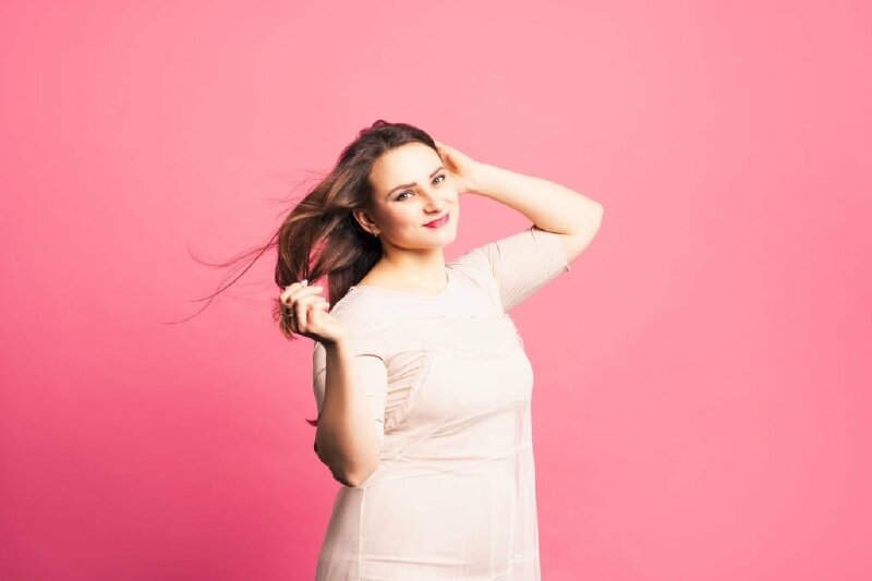 Tạo dáng chụp ảnh đẹp cho các bạn nữ bắp chân to với dáng người hơi nghiêng, 2 tay chạm tóc tạo dáng, mặt hơi nghiêng hướng nhìn ống kính, miệng cười tươi cùng góc chụp nửa người rất dễ thương