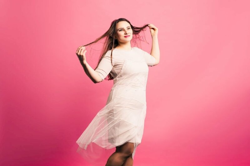 Cách tạo dáng cho các nàng mủm mỉm dễ thương với đầm suông, dáng người đứng hơi nghiêng, 2 tay dơ cao tạo dáng chạm tóc, mặt hơi nghiêng, miệng cười nhẹ, mắt hướng nhìn lên