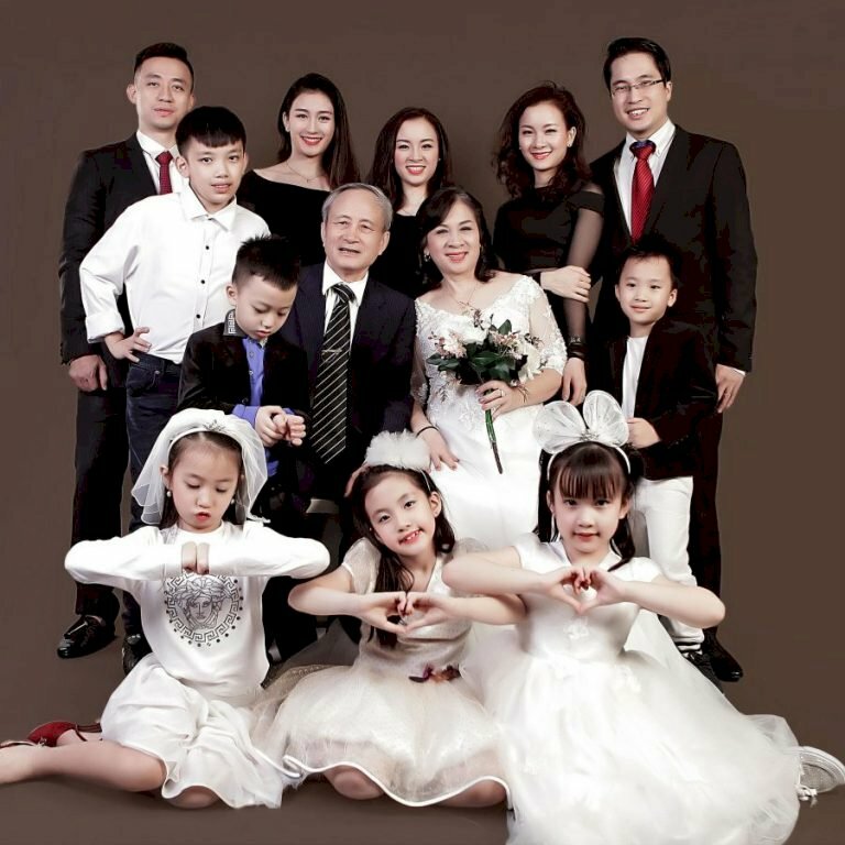 Cách tạo dáng chụp ảnh đại gia đình kiểu Hàn Quốc trên 10 người với ông bà ngồi ghế ở trung tâm, các bé gái ngồi bệt phía trước, tay tạo hình trái tim, ba mẹ của các bé xếp hàng đứng sau lưng ông bà. 