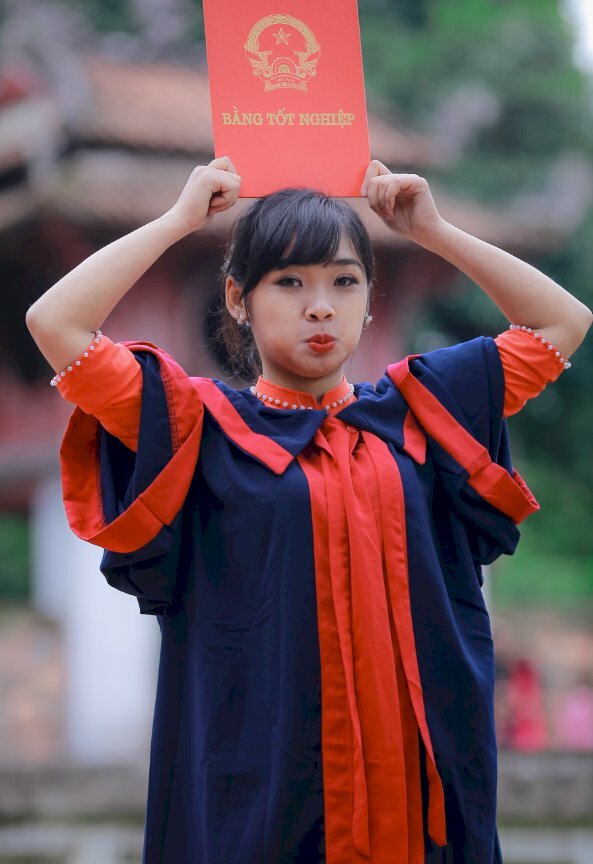 Tạo dáng siêu cute và cá tính với dáng đứng thẳng, 2 tay cầm bằng tốt nghiệp đồi đầu, mắt nhìn ống kính, miệng tạo nét dễ thương