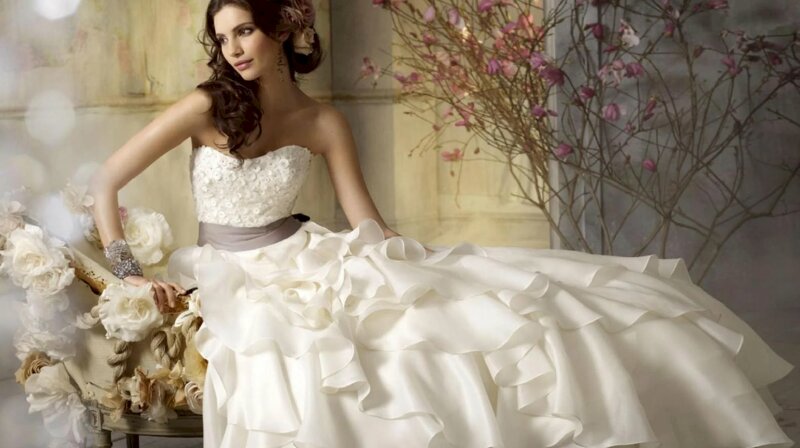 Cách tạo dáng chụp váy cưới khi ngồi bệt tự nhiên, mắt nhìn nghiêng, tay chạm ghế, miệng cười nhẹ