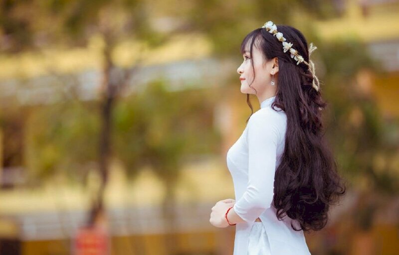 Cách tạo dáng nữ chụp từ góc nghiêng hướng từ dưới lên với đầu đội vòng hoa xinh đẹp 2 tay co chạm nhẹ nhau để trước bụng, miệng vười nhẹ, mắt nhìn về phía trước