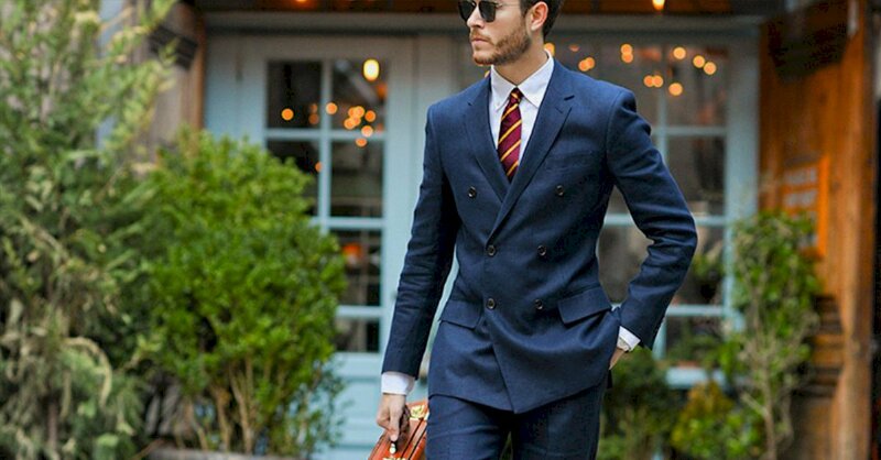 Kiểu tạo dáng nam trong bộ vest xanh tay đặt ở túi quần, tay còn lại cầm túi đồ, mặt hướng về một phía trông lịch lãm và sang trọng