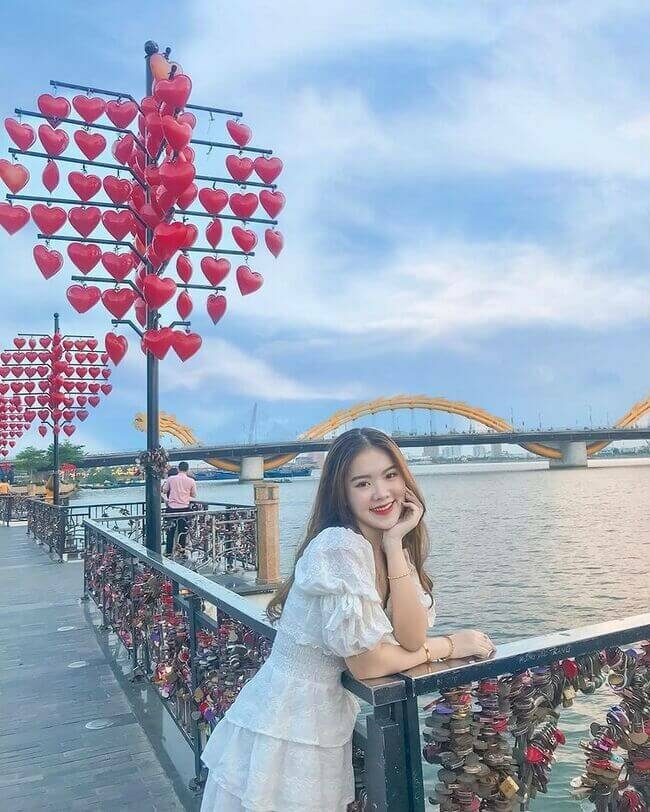 Tạo dáng chụp ảnh ở cầu Tình Yêu vừa lấy được những chiếc chìa khóa tình yêu, vừa có view cầu rồng vừa lấy được cây lồng đèn hình trái tim, với dáng này bạn hãy đứng tựa người vào thành cầu, đặt 1 tay chống nhẹ cằm, 1 tay để trên thành cầu, mỉm cười nhẹ nhìn vào ống kính.