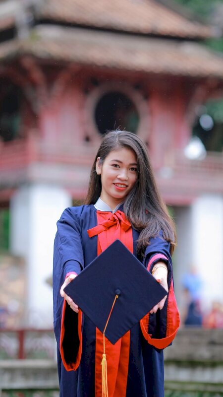 Cách tạo dáng đứng thẳng tự nhiên, 2 tay cầm non cử nhân đưa cao trước ngực về phía ống kính, tóc xõa một bên, miệng cười tươi, mắt nhìn ống kính rất dễ thương