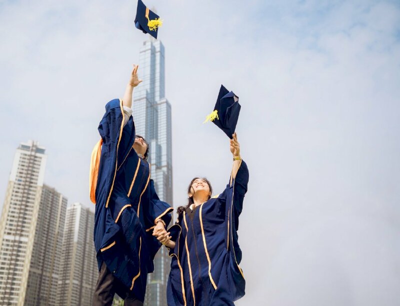 Tạo dáng vui tươi hồ hởi của đôi bạn trẻ cùng đưa tay thảy chiếc nón cử nhân lên cao, tay còn lại nắm chặt tay nhau, mặt hướng lên trời, miệng cười tươi