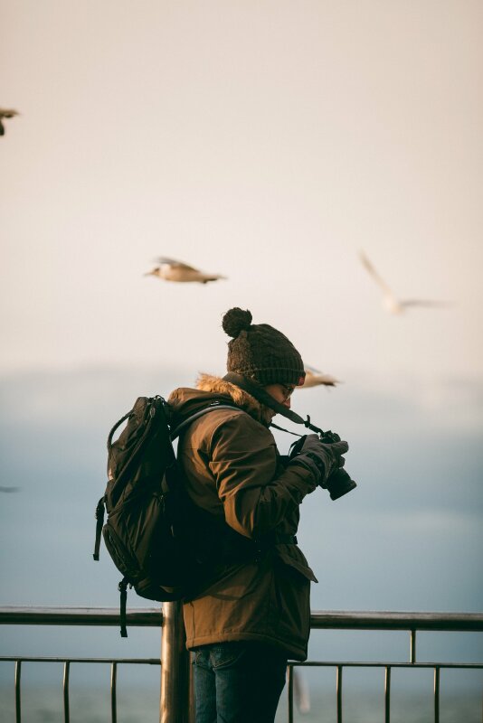 Kiểu chụp ảnh trên cầu cực chất của cô gái trong chiếc áo ấm, nón len cùng chiếc máy ảnh và vai mang balo thể hiện phong cách du lịch năng động, thoải mái