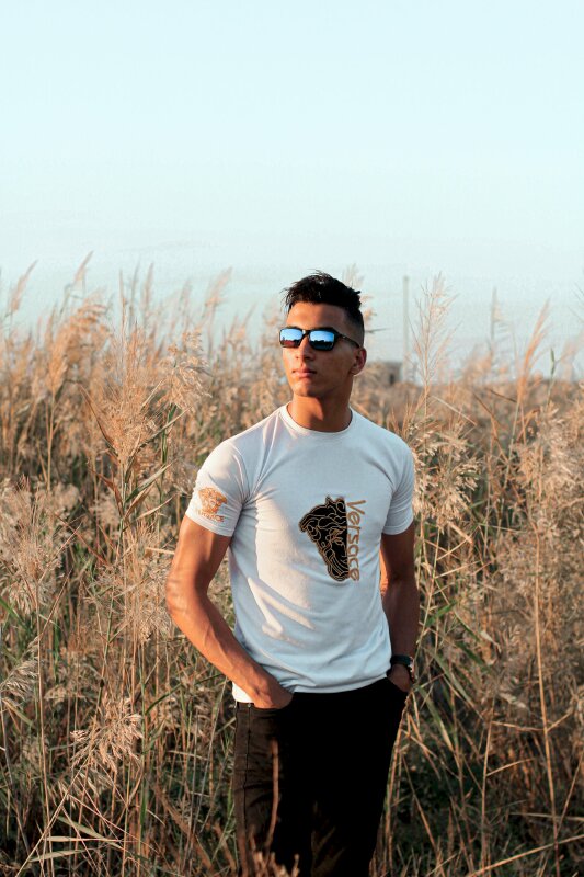 Tạo dáng ngoài trời chất lừ trên cánh đồng cỏ dại trong một buổi chiều nắng vàng, 2 tay đặt túi quần, mặt nhìn nghiêng diễn nét phong cách cùng kính râm siêu ngầu