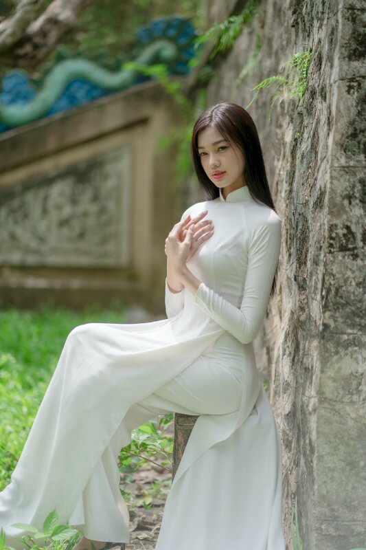 Tạo dáng ngồi tựa vào tường, 2 tay chạm vào nhau đặt lên ngực, mắt nhìn xa, người hơi nghiêng trông rất nghệ thuật