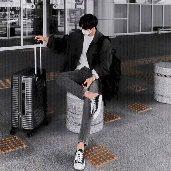 Cách tạo dáng chụp ảnh ở sân bay cho nam ngồi chờ trên ghế đá, với dáng ngồi bắt chân chữ ngũ, một tay đặt lên đùi và tay còn lại cầm vali.
