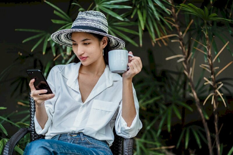 Tạo dáng phong cách quý bà đang nhâm nhi cafe trên tay, tay kia cầm điện thoại, mắt hướng nhìn điện thoại đi cùng với thời trang sang trọng