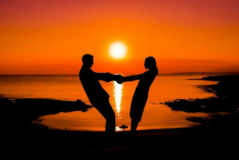 Tạo dáng trên biển của cặp tình nhân đang đứng nắm tay nhau nghiêng người dưới bóng hoàng hôn