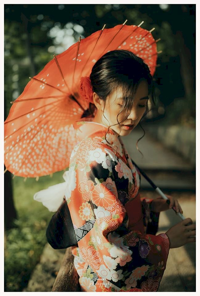 Tạo dáng đứng cực xinh trong chiếc áo hoa Kimono, góc chụp một bên, đầu hơi cúi, mắt nhìn xuống, 2 tay cầm dù tựa lên vai